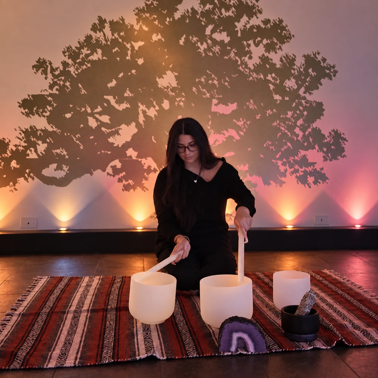 Sylvia Lee playing white singing bowls in front of a tree mural